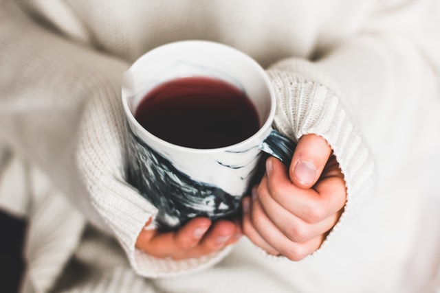 Person wearing a cosy white jumper is holding a cup of tea in their hands