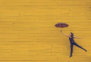 A person holding an umbrella jumps in front of a yellow brick wall