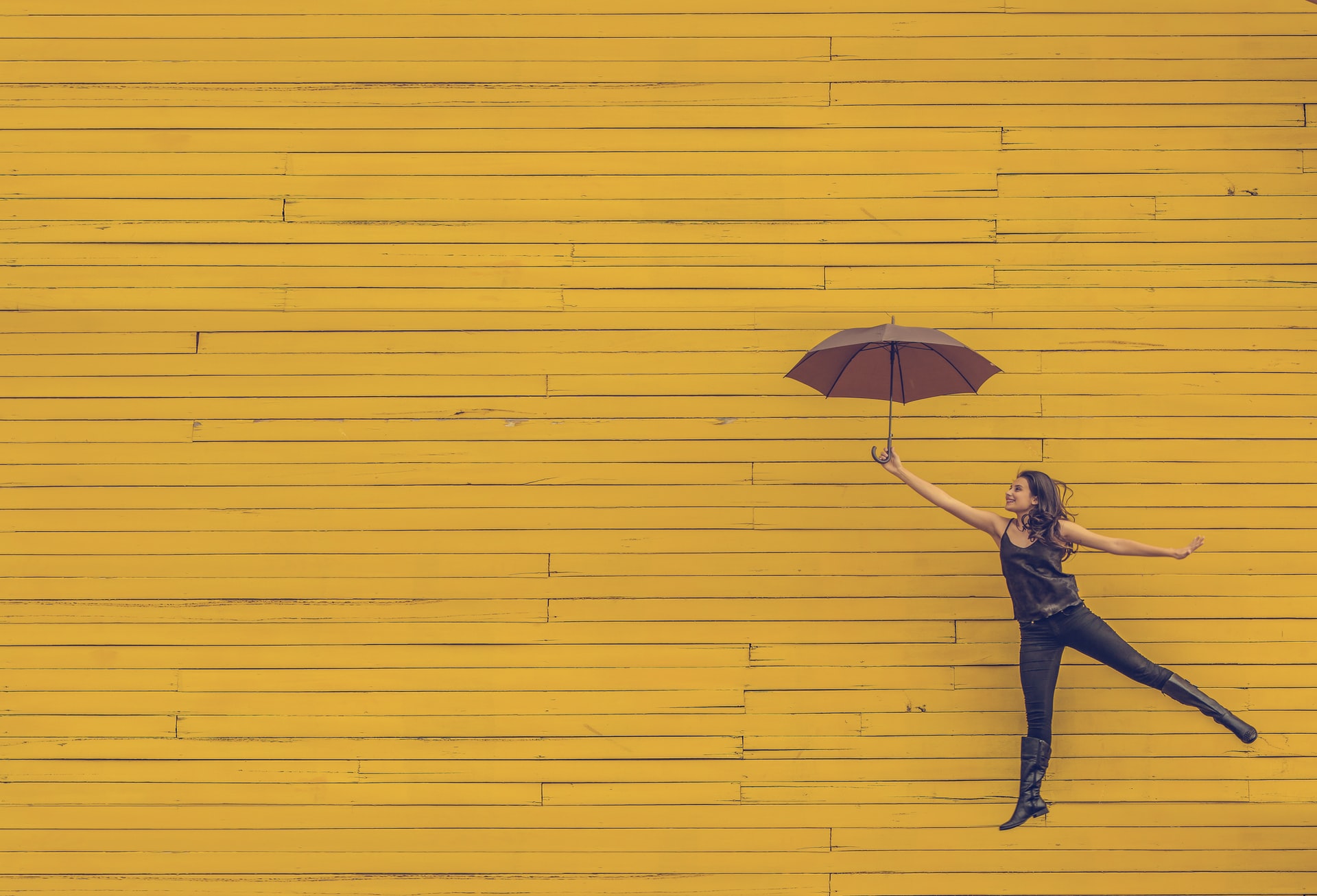 A person holding an umbrella jumps in front of a yellow brick wall