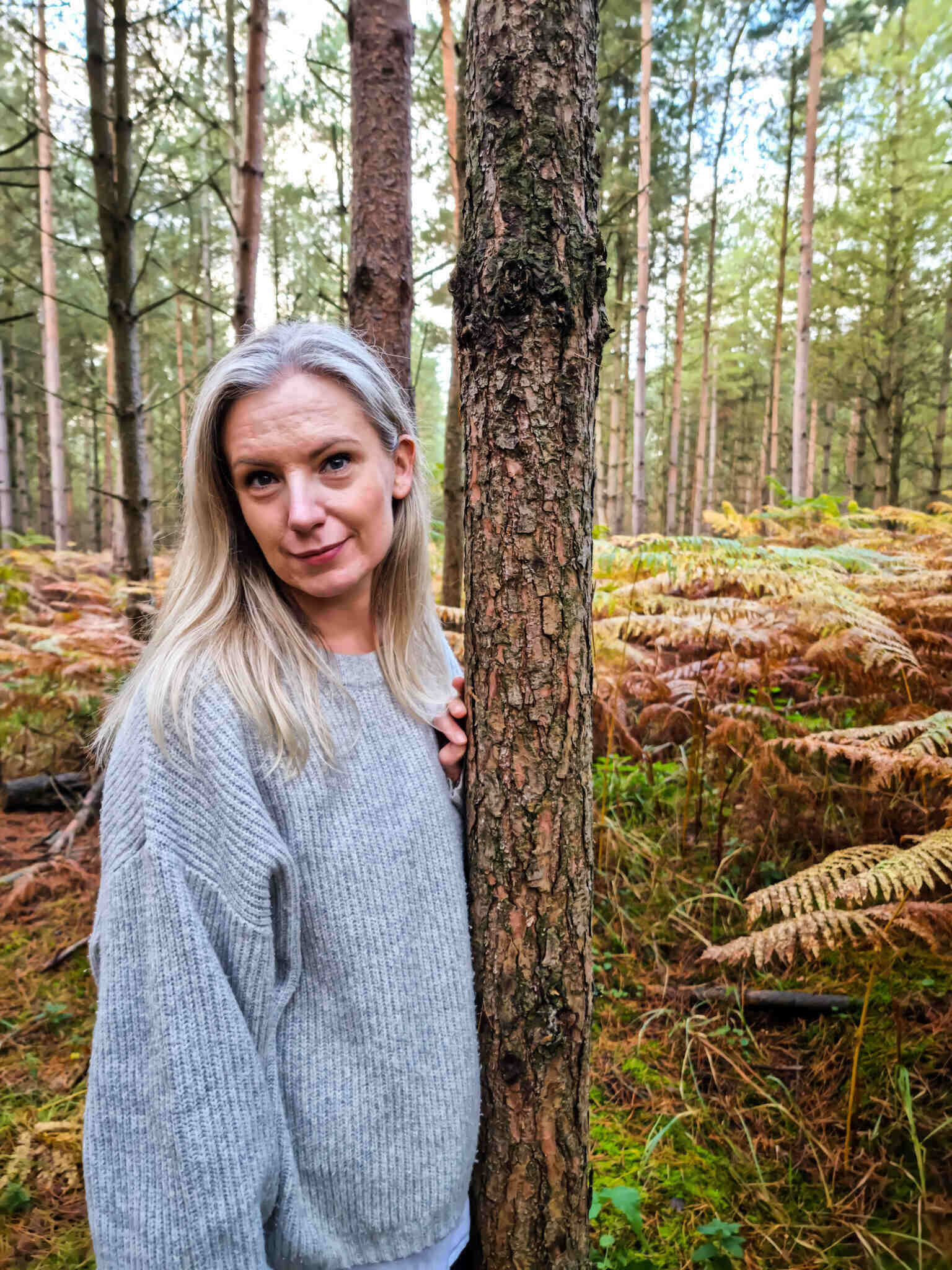 Sarah is standing in a forest next to a tree with golden ferns around her